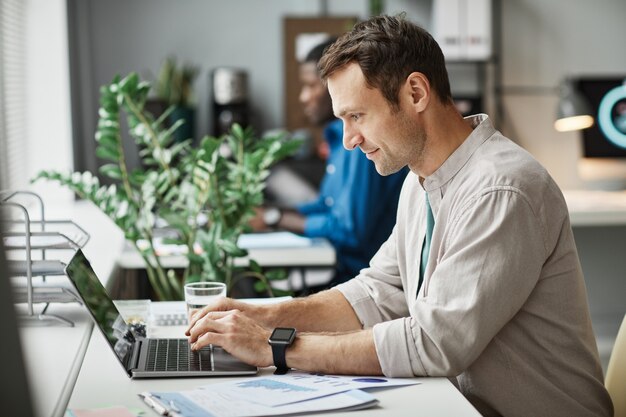 side-view-portrait-smiling-adult-man-using-laptop-while-enjoying-work-office-copy-space_236854-34428